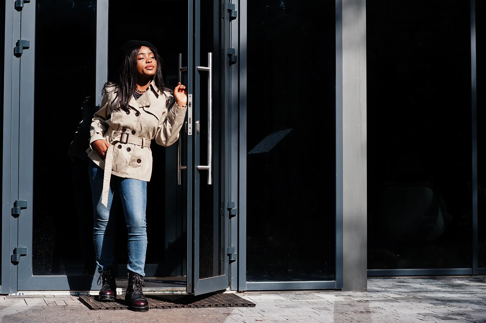 woman in short trench style jacket leaning against open pedestrian door