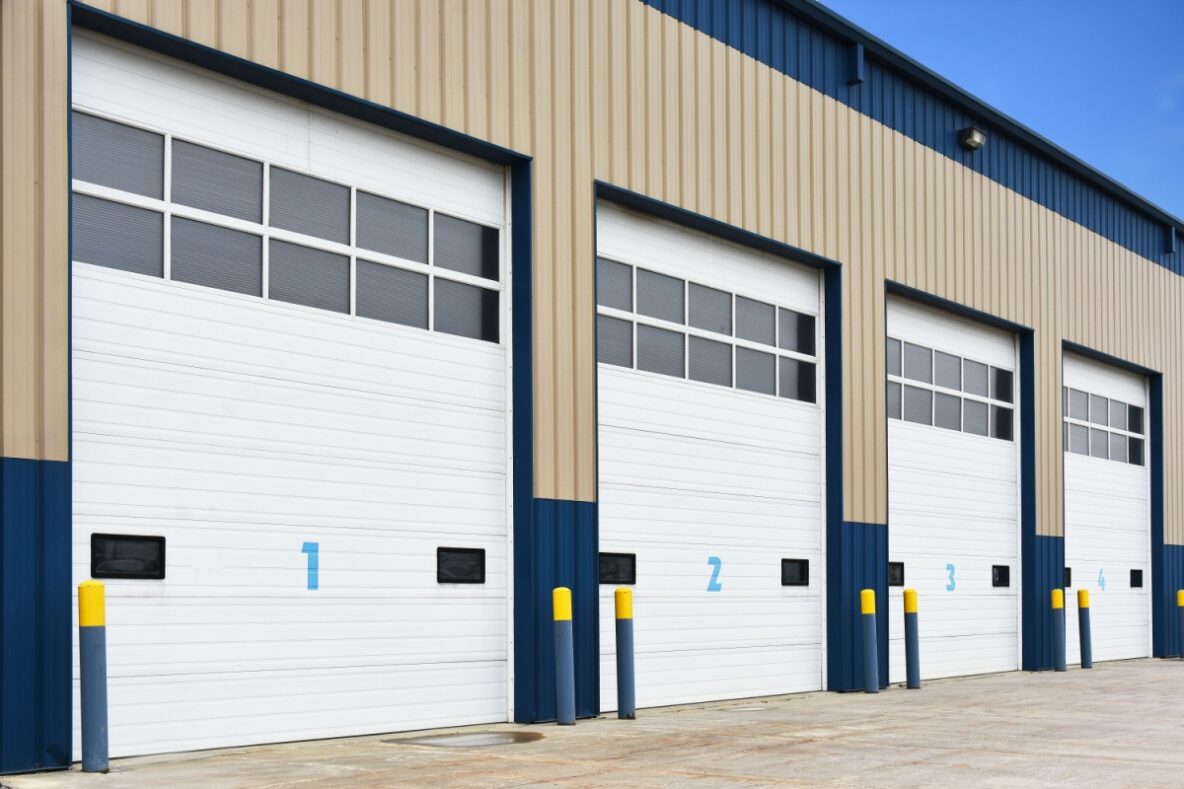 Closed commercial overhead doors on a tan and blue building